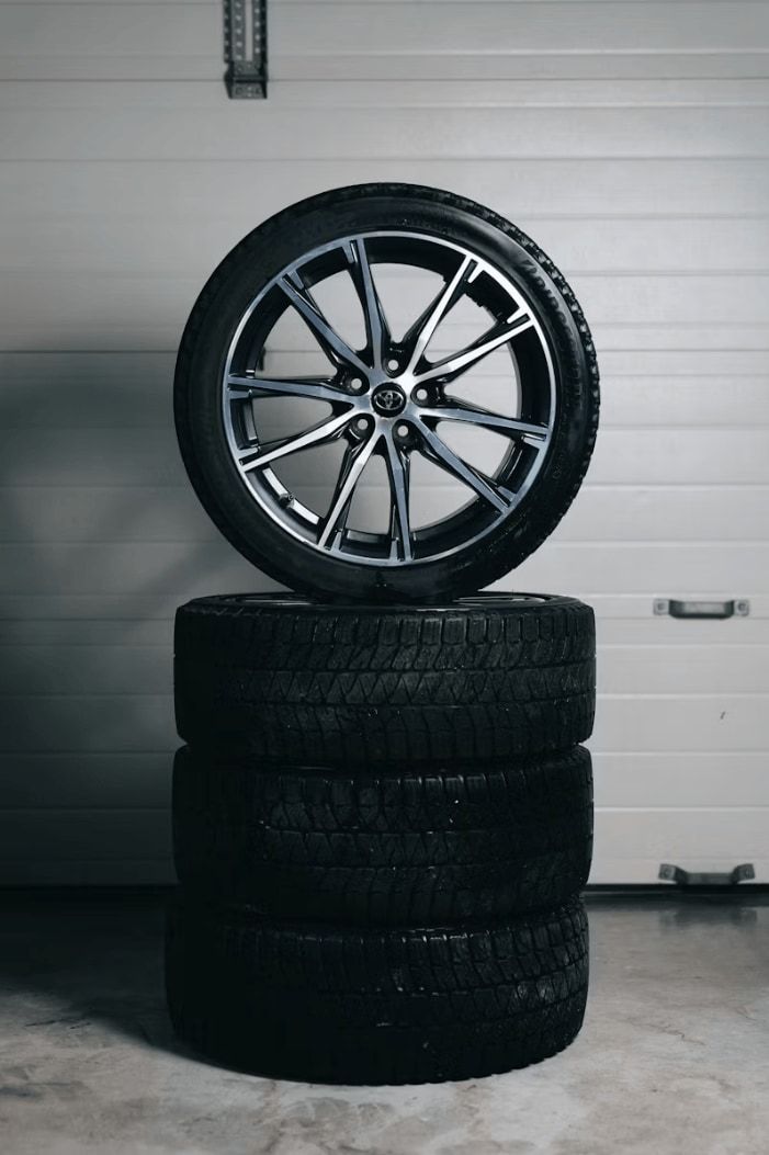 Alloy wheel and tire resting on a stack of tires in front of a garage door